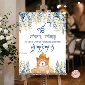 May include: A white sign with blue and white floral accents. The sign has the text "Satnaam Waheguru" in Punjabi, followed by a line of text in Punjabi, and then "Ji Aayan Nu" in Punjabi. The sign also features a small illustration of a golden temple.