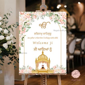 May include: A white welcome sign with floral borders and gold accents. The sign features the text "Satnam Waheguru" in Punjabi, followed by "Welcome ji" and "ji ayian nu" in English and Punjabi. The sign also includes a small illustration of a golden temple with a figure inside.