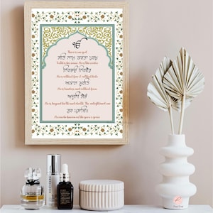 Może przedstawiać: Wydruk w ramie z ozdobną ramką w kolorze zielonym, złotym i białym. Wydruk zawiera tekst w języku pendżabskim, który tłumaczy się jako "Jest jeden Bóg. Prawda jest jego imieniem. On jest stwórcą. On jest bez strachu i bez nienawiści. On jest ponadczasowy i bez formy. On jest poza narodzinami i śmiercią. Oświecony może być znany jako łaska guru."