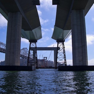 May include: A view of a large concrete bridge under construction. The bridge is made of large concrete beams and supports. The bridge is over a body of water.