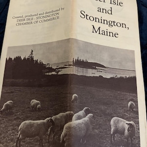 May include: A black and white photo of a field with sheep grazing. The photo is from a brochure welcoming visitors to Deer Isle and Stonington, Maine.