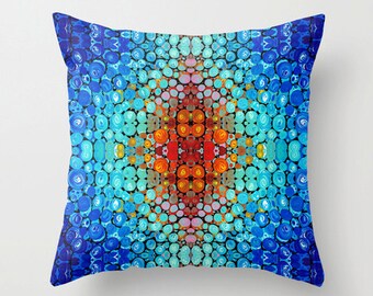 May include: Square throw pillow with a vibrant, abstract design. The pattern features a central burst of orange and red, surrounded by concentric circles of blue and turquoise hues. The overall effect is a colorful, eye-catching design.