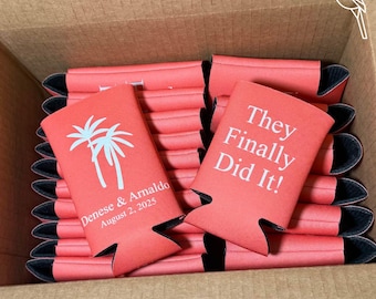 May include: A stack of coral-colored can coolers with black trim. One cooler displays the text "They Finally Did It!" in white. Another cooler shows two palm trees and the names "Denese & Arnaldo" and the date "August 2, 2025".