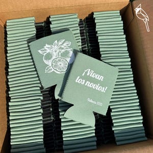 May include: A stack of light green can coolers with a white citrus fruit design and the text "¡Vivan los novios!" and "Valencia 2025". The coolers are made of a foam material and are in a cardboard box.