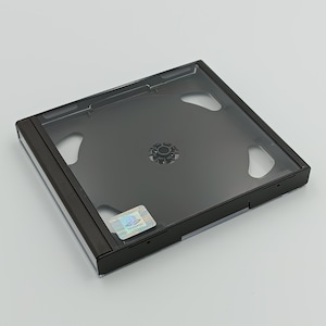 Op de afbeelding: Zwarte plastic CD-doos met een transparant plastic deksel voor een CD of DVD. De doos heeft een PlayStation-logo sticker op de voorkant.