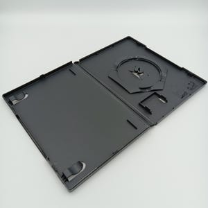 Peut inclure: Boîtier DVD en plastique noir avec un porte-disque en plastique transparent. Le boîtier est ouvert et le porte-disque est visible.