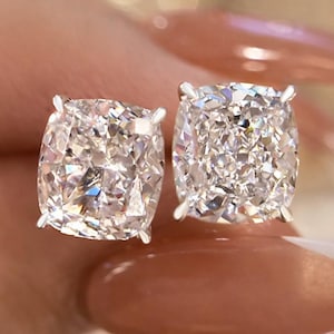 May include: A pair of square-cut diamond stud earrings. The diamonds are set in a silver or white gold setting. The earrings are shown close up, highlighting the sparkle and clarity of the gemstones.