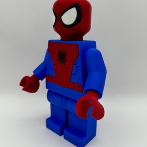 May include: A large, stylized Spider-Man figure in a blocky design. The figure features a red head and hands, with white eyes outlined in black. The torso is red with a black spider emblem, and the arms and legs are blue.