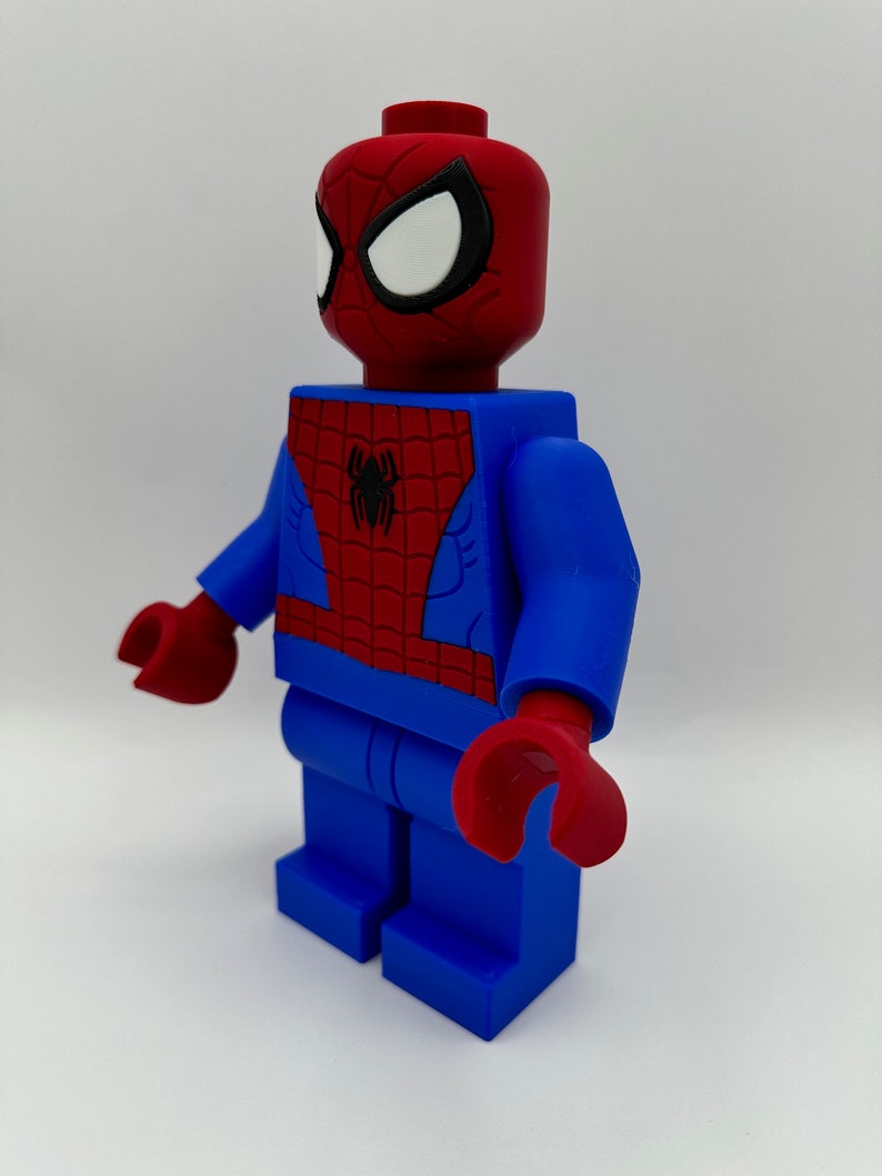 May include: A large, stylized Spider-Man figure in a blocky design. The figure features a red head and hands, with white eyes outlined in black. The torso is red with a black spider emblem, and the arms and legs are blue.