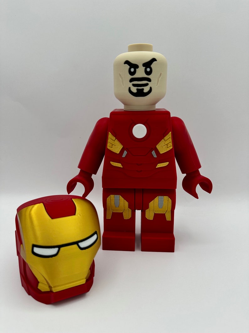 May include: A red and gold Lego minifigure of Iron Man with a stern expression. The minifigure is wearing a red and gold suit with a white circle on the chest. The minifigure is holding a separate red and gold Lego helmet.