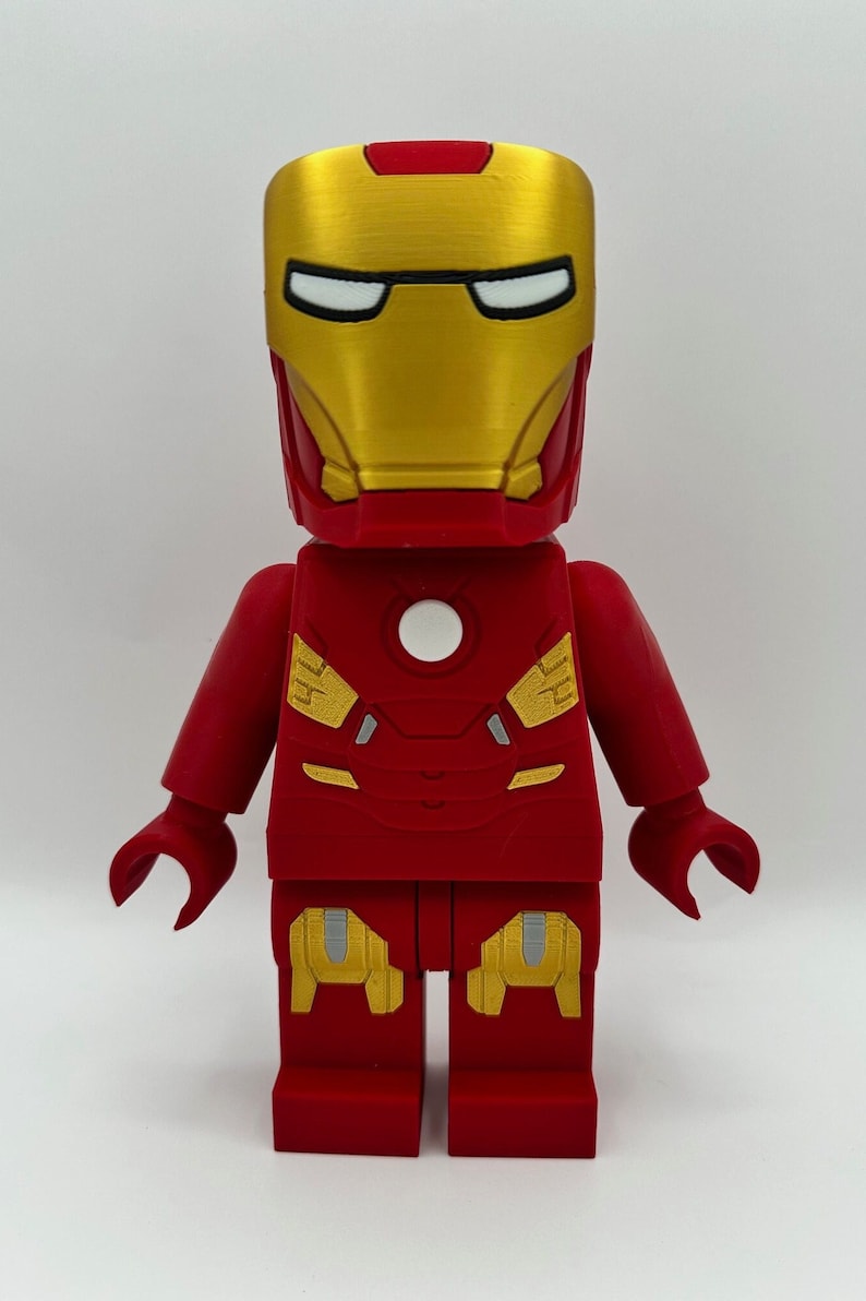 May include: A red and gold Lego minifigure of Iron Man. The figure has a detailed head with a gold mask and a red chest piece with a white arc reactor.