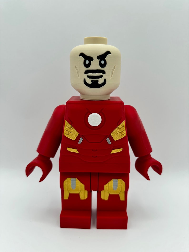 May include: A red and gold Lego minifigure of Iron Man. The minifigure has a white face with black eyes and a black mustache. The minifigure is wearing a red and gold suit with a white circle on the chest.