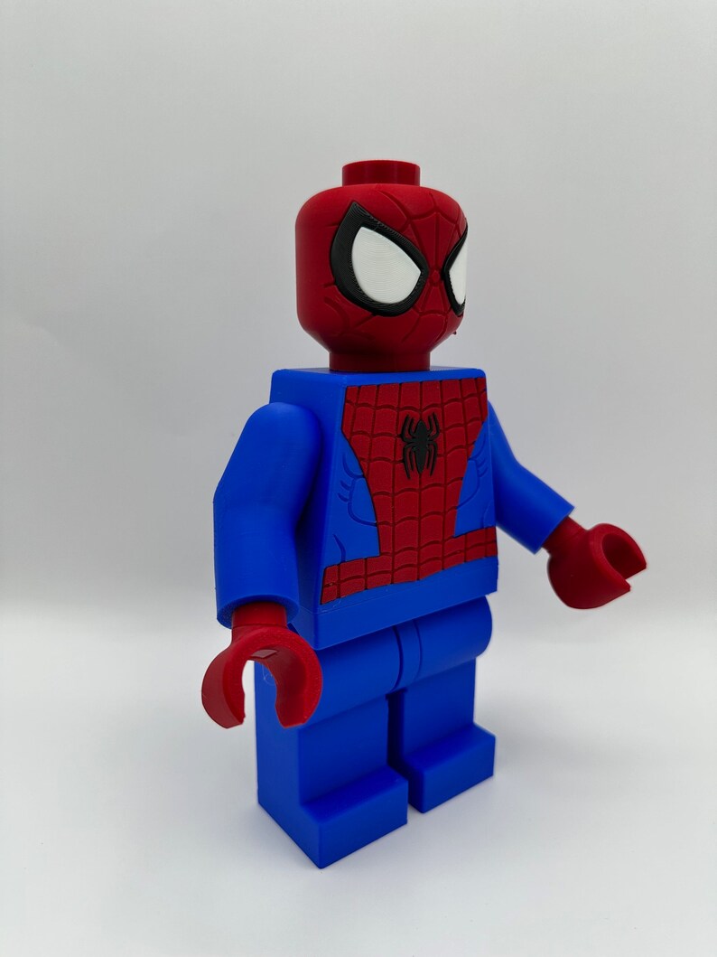 May include: A large, blue and red Spider-Man figure, resembling a Lego minifigure. The figure has a red head with white eyes and a black outline, and a red and blue torso with a black spider emblem. The hands are red.