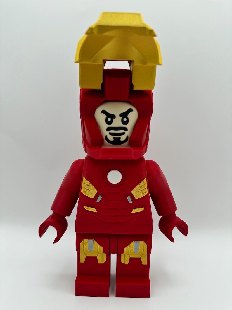 May include: A red and yellow Lego minifigure of Iron Man with a white face and a black mustache. The minifigure has a yellow helmet with a red visor and a red chest plate with a white circle in the center.