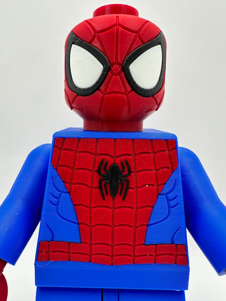 May include: A red, blue, and black Spider-Man figure. The figure has a red head with white eyes and a black outline. The torso is blue with a red spiderweb design and a black spider emblem. The arms are blue.