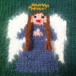 May include: Knitted angel ornament with white wings, a blue dress, brown hair, and a yellow halo. The angel is smiling.