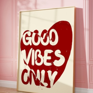 May include: A white framed canvas print with a red heart shape. The heart has the words "GOOD VIBES ONLY" written in white inside of it.