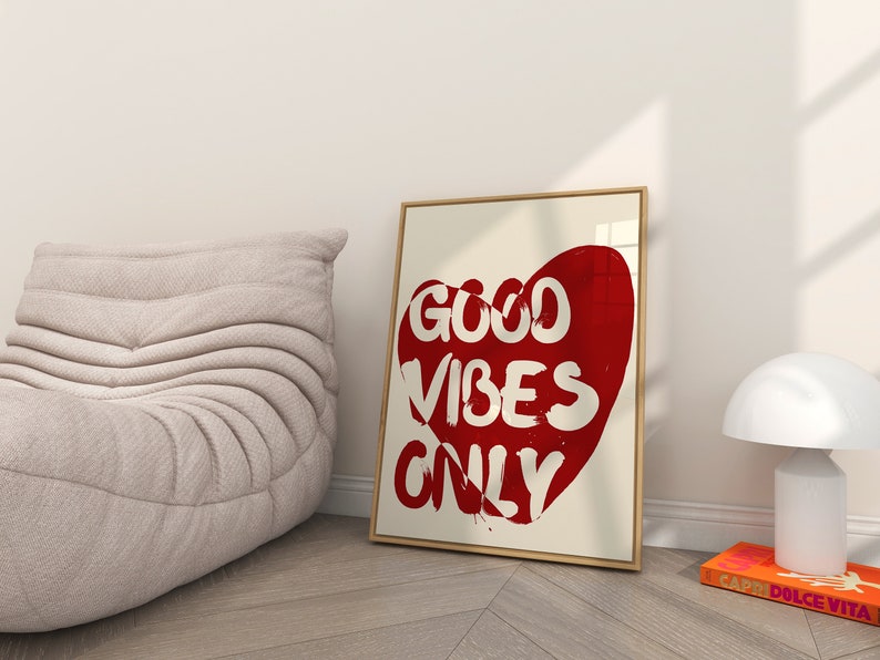 May include: A framed print with a red heart shape containing the text "GOOD VIBES ONLY" in white lettering. The print is hanging on a white wall.