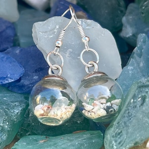 May include: A pair of silver dangle earrings with clear glass globes filled with sand and seashells.