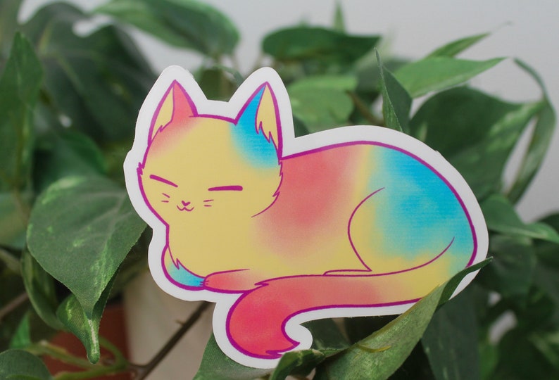 Sticker of a cat with a yellow base and blue and pink spots representing the pansexual flag.