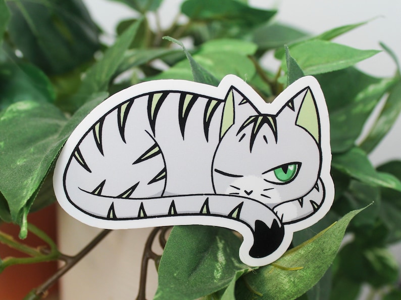 Sticker of a cat with an orange base and green and black stripes representing the aromantic flag.