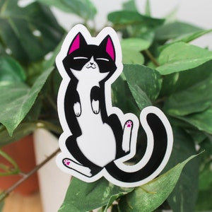 Sticker of a cat on its back with a tuxedo pattern and purple ears representing the asexual flag.