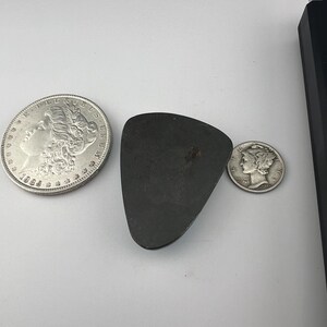 May include: A silver dollar coin with the year 1885, a silver half dollar coin, and a dark gray triangular shaped stone.