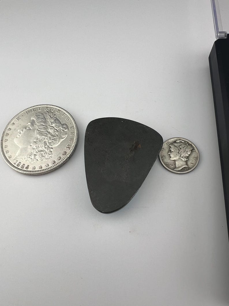 May include: A silver dollar coin with the year 1885, a silver half dollar coin, and a dark gray triangular shaped stone.