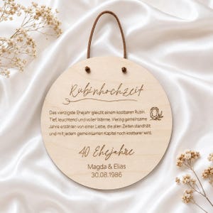 Könnte beinhalten: Ein rundes Holzschild mit einem braunen Lederband zum Aufhängen. Der Text lautet "Rubinhochzeit", gefolgt von einem Gedicht zum 40. Hochzeitstag, dem Text "40 Ehejahre" sowie den Namen "Magda & Elias" und dem Datum "30.08.1986".