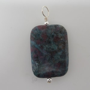 May include: A rectangular pendant made of a dark green and pink stone with a silver bail.