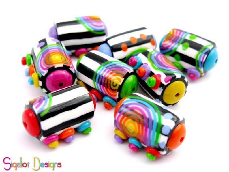 May include: A collection of colorful, handmade polymer clay beads. The beads are cylindrical with black and white striped patterns, rainbow swirls, and various colored accents. The ends of the beads are brightly colored, with pink, red, yellow, and blue details.
