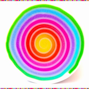 May include: A colorful, spiral-shaped object with a rainbow of hues, including yellow, red, pink, purple, blue, and green. The design is centered on a white surface, with a striped border in various colors.