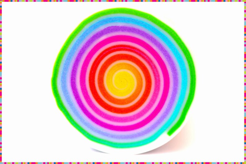 May include: A colorful, spiral-shaped object with a rainbow of hues, including yellow, red, pink, purple, blue, and green. The design is centered on a white surface, with a striped border in various colors.