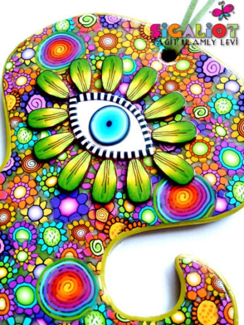 May include: A colorful, handcrafted decorative piece with a floral design and an eye-shaped centerpiece. The piece features a vibrant mix of colors, including green, blue, yellow, orange, and purple. The text "SIGALIOT SAGIT BRAMLY LEVI" is visible.