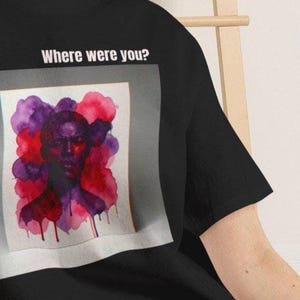 Könnte beinhalten: Ein schwarzes Kurzarm-T-Shirt mit einem Grafikdruck eines Gesichts, das von violetten und roten aquarellartigen Farbspritzern umgeben ist. Über der Grafik ist der Text "Where were you?" in weißen, serifenlosen Großbuchstaben aufgedruckt.