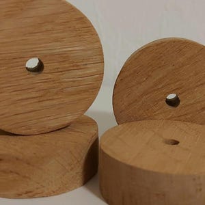 Könnte beinhalten: Vier unfertige Holzspielzeugräder. Zwei Räder stehen aufrecht, zwei liegen flach. Jedes Rad hat ein Loch in der Mitte. Die Holzmaserung ist sichtbar, und die Räder sind hellbraun.