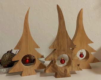 May include: Three wooden Christmas tree ornaments with a cutout in the center to hold a small red ornament. The trees are made of natural wood and have a rustic look.