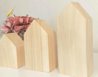 May include: Three wooden houses of varying sizes, all made of light wood with a natural grain. The houses are arranged in a row from smallest to largest.
