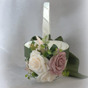 May include: A white satin flower girl basket with a green satin ribbon and a bouquet of white and blush pink roses with greenery.