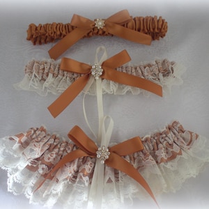 May include: Three bridal garters with brown satin ribbon and lace trim. Each garter features a rhinestone embellishment.
