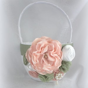 May include: A white flower girl basket with a green satin ribbon and a pink fabric flower with pearl accents.