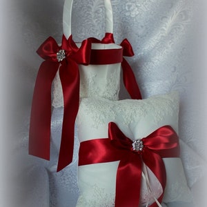 May include: A white lace ring pillow and a white lace flower girl basket with red satin ribbon and a rhinestone embellishment.