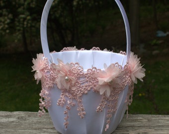 May include: White flower girl basket with a pink lace trim and pink fabric flowers. The basket is sitting on a wooden railing.
