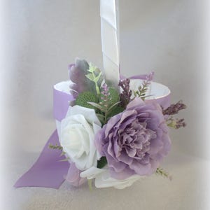 May include: A white flower girl basket with a lavender satin ribbon and a bouquet of white and lavender flowers.