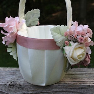 May include: A white satin flower girl basket with a pink satin ribbon and pink and white flowers.