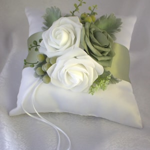 May include: White satin ring pillow with a green satin ribbon and a floral arrangement of white and green roses.