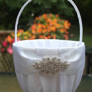 May include: White satin flower girl basket with a silver rhinestone embellishment. The basket has a white satin ribbon handle.