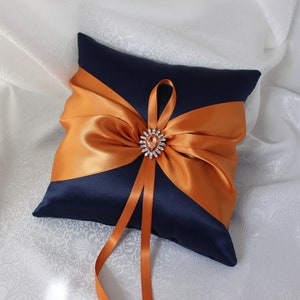 May include: A navy blue satin ring pillow with a large orange satin bow and a jeweled brooch in the center.