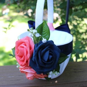 May include: A white flower girl basket with a navy blue ribbon and coral and navy blue silk flowers.