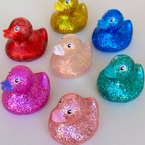 May include: Six glitter rubber duck toys in various colors: red, yellow, blue, pink, light pink, and teal.